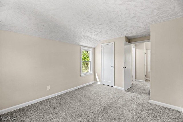 carpeted empty room with a textured ceiling, vaulted ceiling, and baseboards