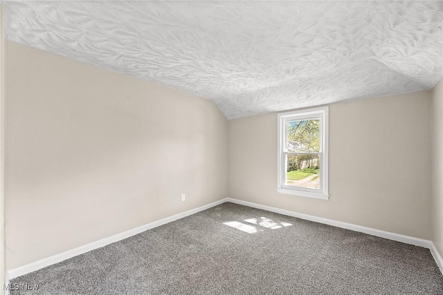carpeted empty room featuring baseboards, a textured ceiling, and vaulted ceiling