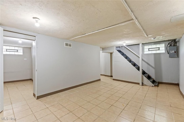 basement featuring a healthy amount of sunlight, stairs, a textured ceiling, and visible vents