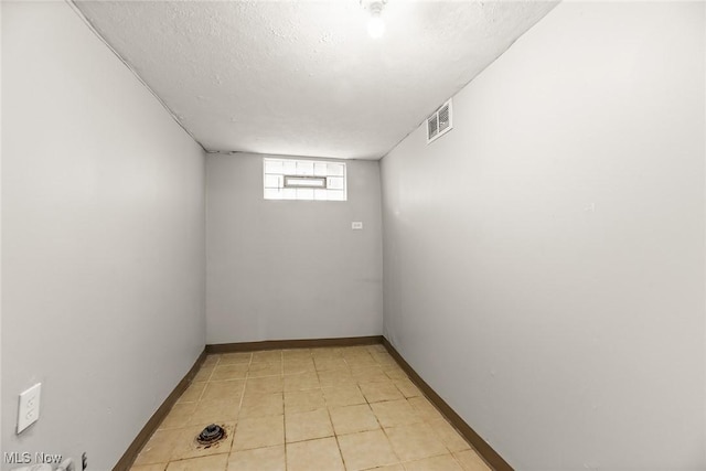 empty room with light tile patterned floors, baseboards, a textured ceiling, and visible vents