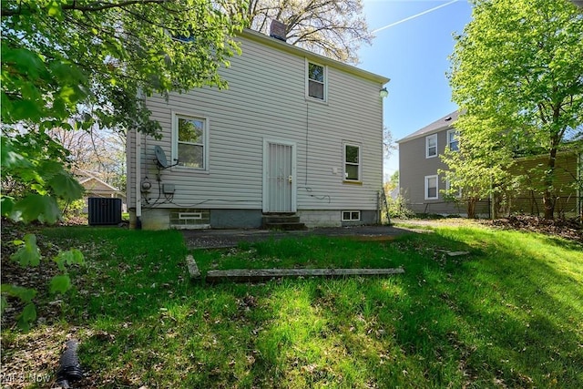 back of house featuring a chimney, a lawn, central AC unit, fence, and entry steps