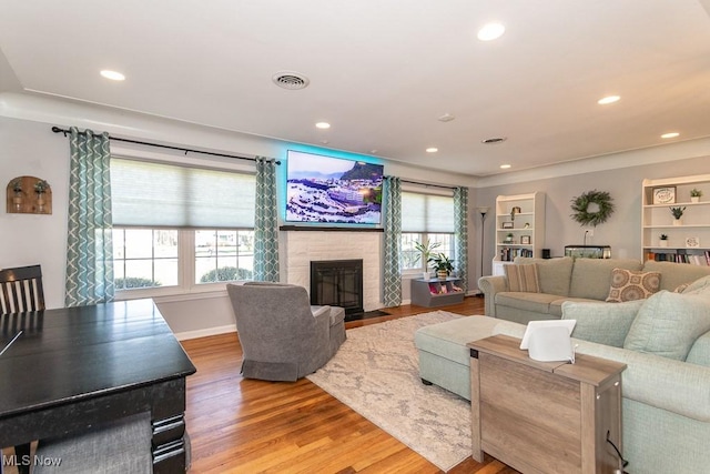 living area featuring recessed lighting, visible vents, a fireplace with flush hearth, and wood finished floors