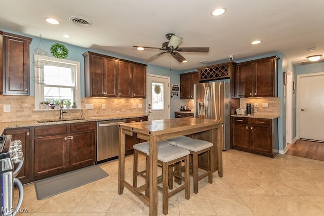 kitchen featuring visible vents, appliances with stainless steel finishes, tasteful backsplash, light stone countertops, and a sink