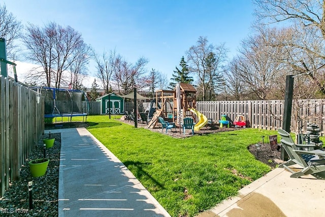view of play area with a trampoline, a lawn, an outbuilding, a fenced backyard, and a storage unit