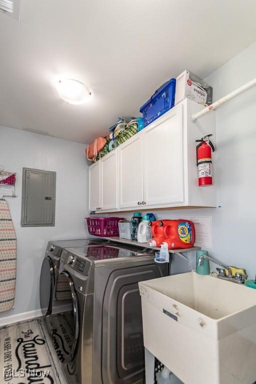 washroom featuring baseboards, electric panel, separate washer and dryer, a sink, and cabinet space