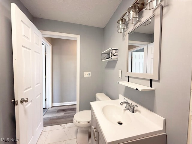 half bathroom with toilet, baseboards, marble finish floor, and vanity