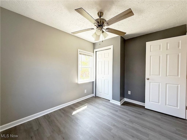 unfurnished bedroom featuring ceiling fan, a textured ceiling, baseboards, a closet, and dark wood-type flooring