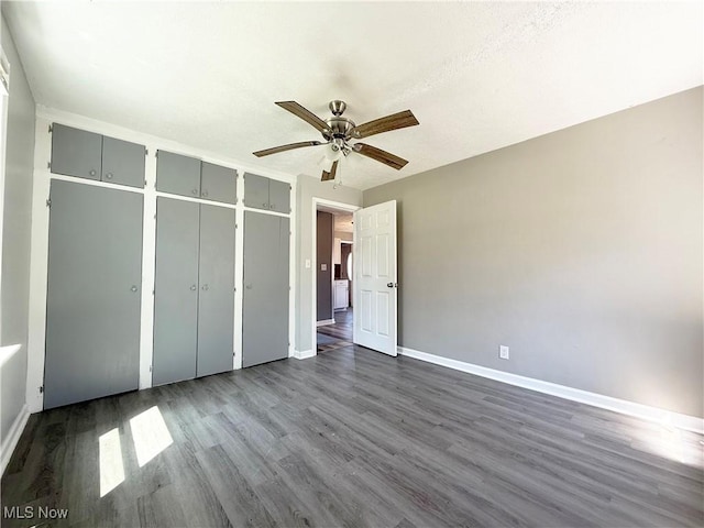 unfurnished bedroom with baseboards, a ceiling fan, and dark wood-type flooring