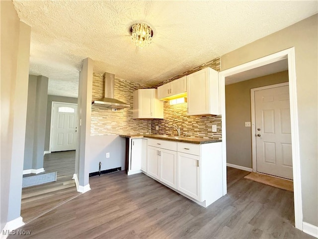 kitchen with light wood-style floors, baseboards, wall chimney range hood, and white cabinetry