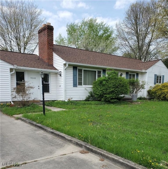 ranch-style home with roof with shingles, a chimney, and a front lawn