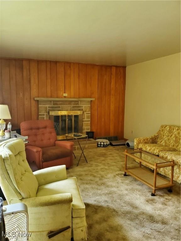 carpeted living room featuring wood walls and a stone fireplace