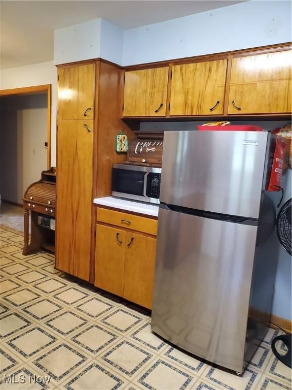 kitchen with brown cabinetry, light countertops, light floors, and appliances with stainless steel finishes