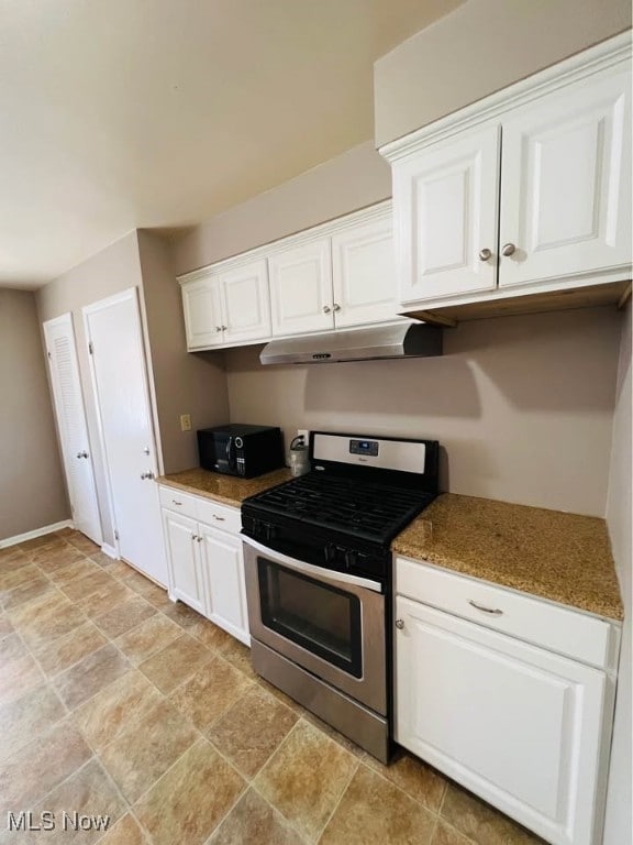 kitchen with under cabinet range hood, white cabinets, stone finish floor, and stainless steel gas range oven