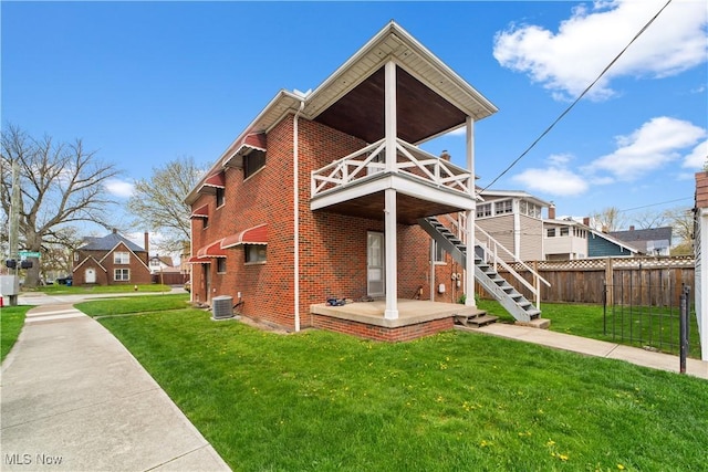 view of front of house featuring brick siding, fence, central air condition unit, and a front yard