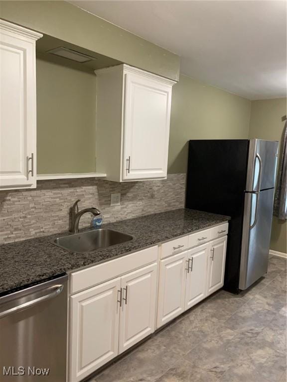 kitchen with white cabinets, a sink, dark stone countertops, stainless steel appliances, and decorative backsplash