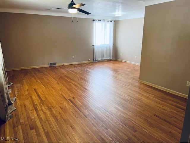 spare room with a ceiling fan, baseboards, visible vents, and wood finished floors