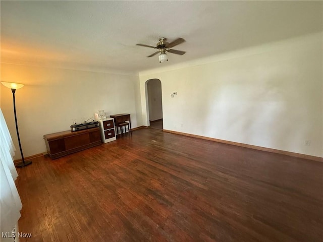 empty room with arched walkways, ceiling fan, dark wood-style floors, and baseboards