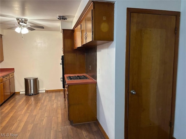 kitchen featuring brown cabinets, dark wood-style flooring, ceiling fan, stainless steel gas cooktop, and baseboards