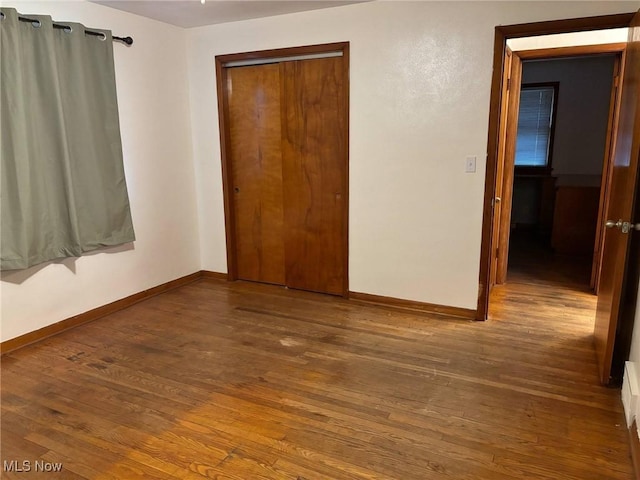 unfurnished bedroom with baseboards, a closet, and hardwood / wood-style flooring