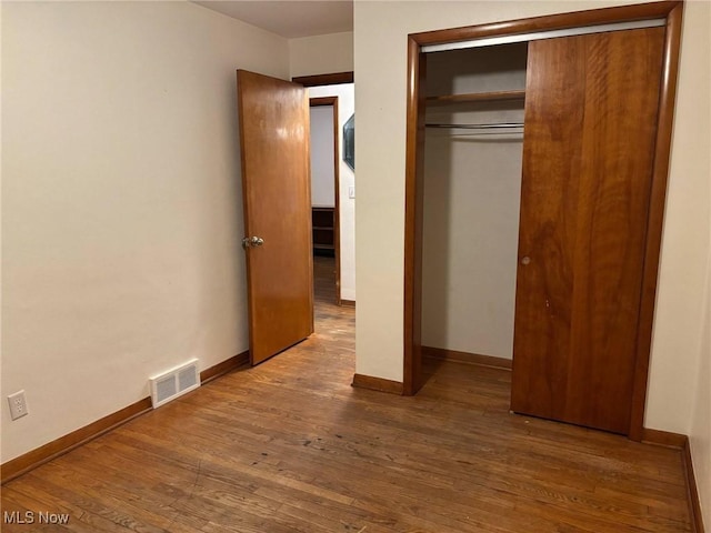 unfurnished bedroom with baseboards, visible vents, wood finished floors, and a closet