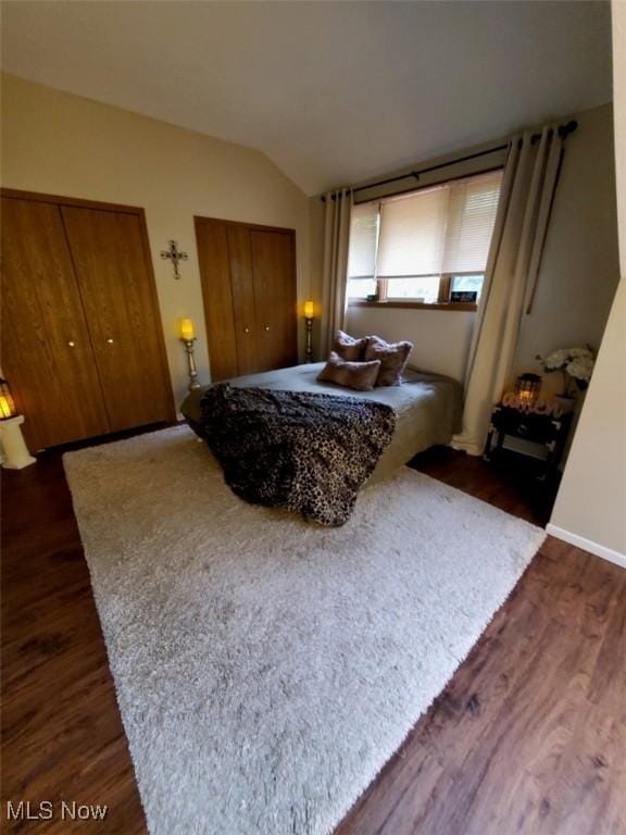 bedroom featuring two closets, dark wood-style flooring, and lofted ceiling