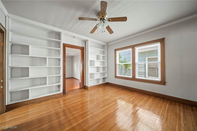 spare room featuring ornamental molding, baseboards, built in shelves, a ceiling fan, and light wood finished floors