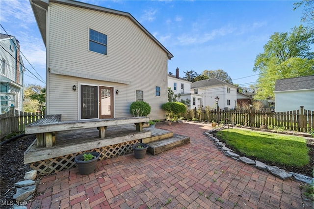 rear view of property with fence, a wooden deck, and a patio area