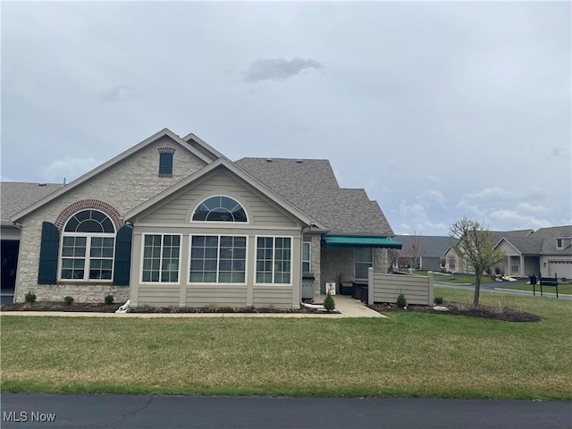 view of front facade featuring roof with shingles, stone siding, and a front lawn