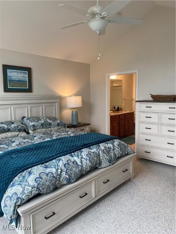 bedroom featuring a ceiling fan, light colored carpet, lofted ceiling, and ensuite bath