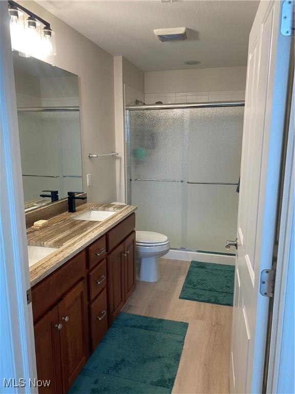 bathroom featuring double vanity, a stall shower, wood finished floors, a sink, and toilet