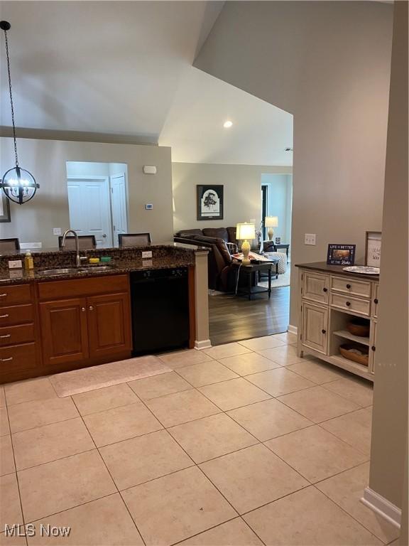 kitchen with light tile patterned flooring, hanging light fixtures, a sink, dark stone countertops, and black dishwasher
