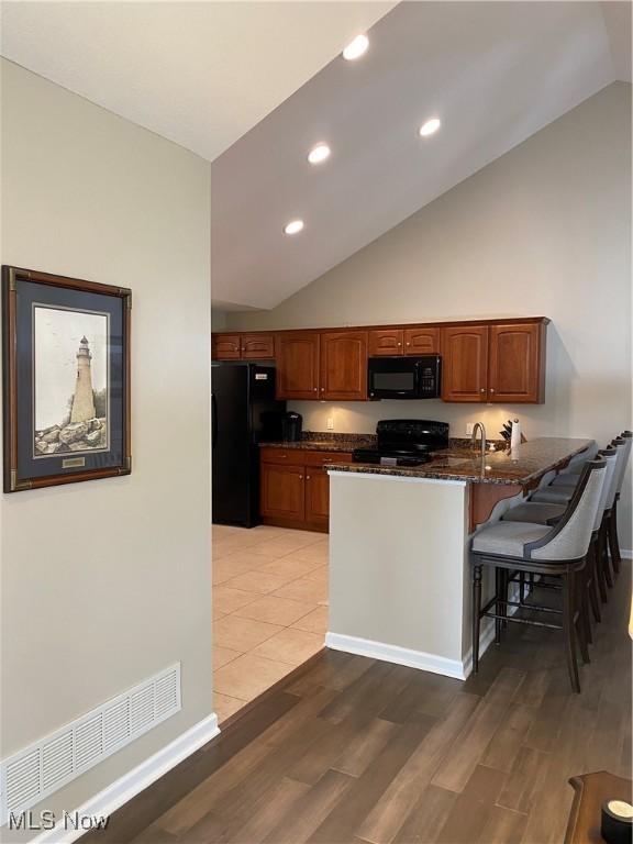 kitchen with light wood finished floors, a peninsula, black appliances, and a kitchen breakfast bar