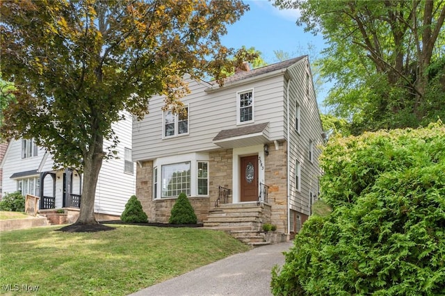 view of front of property featuring driveway, a front lawn, and stone siding