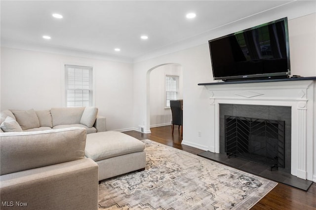 living room featuring arched walkways, a fireplace, dark wood finished floors, baseboards, and recessed lighting