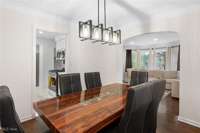 dining space with arched walkways, baseboards, and dark wood finished floors