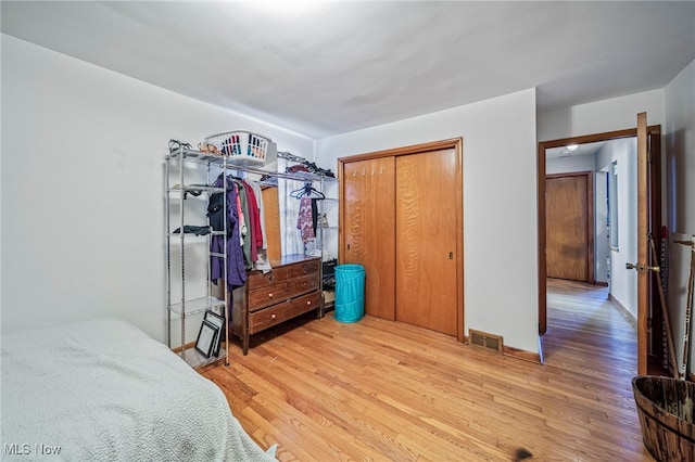 bedroom with baseboards, visible vents, light wood finished floors, and a closet