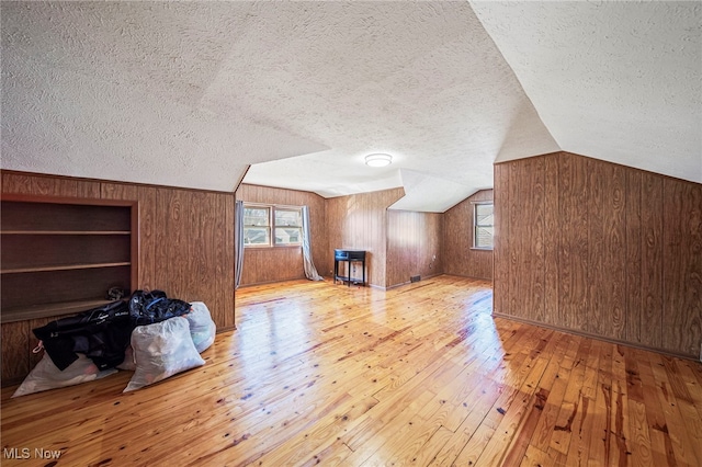 additional living space with a textured ceiling, wood walls, a healthy amount of sunlight, and hardwood / wood-style floors