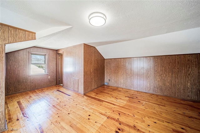 additional living space with wooden walls, a textured ceiling, light wood finished floors, and lofted ceiling