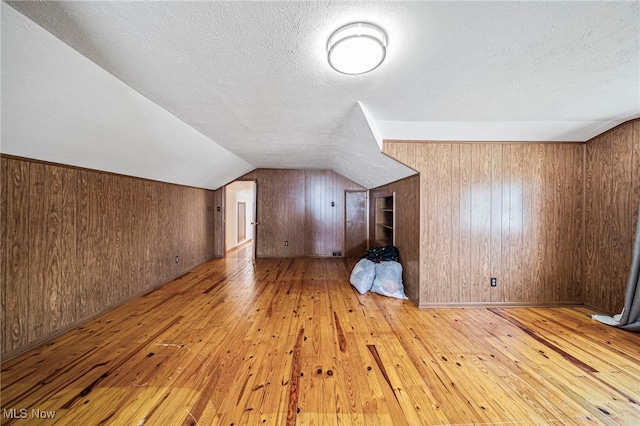 bonus room featuring wood-type flooring, a textured ceiling, wood walls, and vaulted ceiling