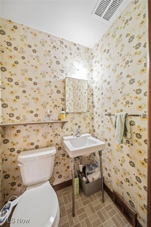 half bathroom featuring toilet, wallpapered walls, and baseboards