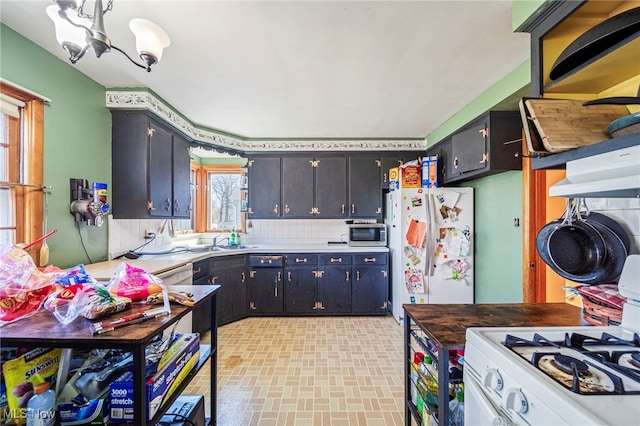 kitchen with decorative backsplash, light countertops, a notable chandelier, under cabinet range hood, and white appliances