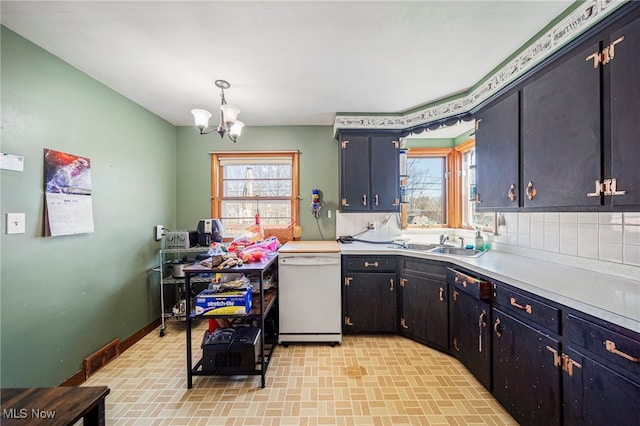 kitchen featuring brick patterned floor, white dishwasher, light countertops, tasteful backsplash, and a notable chandelier