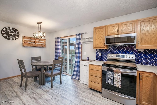 kitchen with light wood-style floors, light countertops, appliances with stainless steel finishes, and backsplash