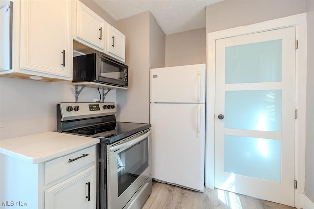 kitchen with stainless steel range with electric cooktop, black microwave, light wood finished floors, freestanding refrigerator, and white cabinetry