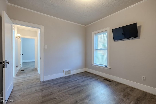 empty room with visible vents, crown molding, wood finished floors, baseboards, and a textured ceiling
