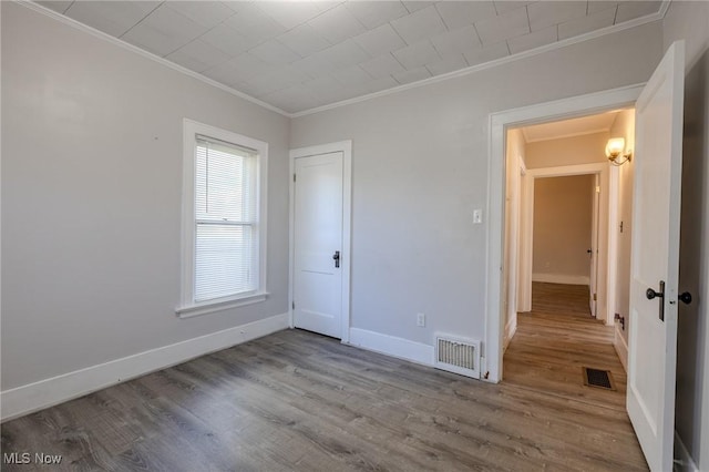 unfurnished bedroom featuring baseboards, visible vents, ornamental molding, and wood finished floors