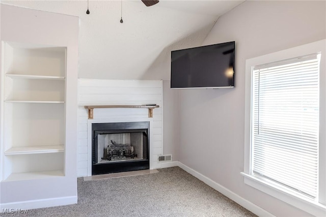unfurnished living room with a ceiling fan, visible vents, a fireplace, vaulted ceiling, and carpet floors