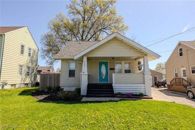 bungalow-style home with a front lawn, fence, covered porch, roof with shingles, and central air condition unit