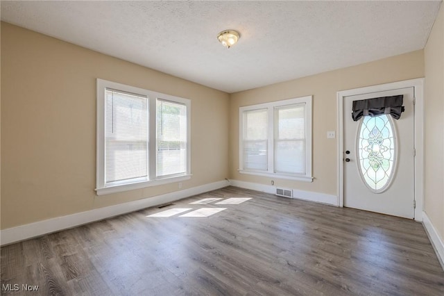 foyer featuring visible vents, a textured ceiling, baseboards, and wood finished floors