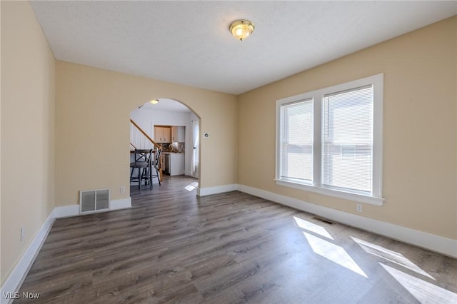 unfurnished room with visible vents, arched walkways, baseboards, and wood finished floors